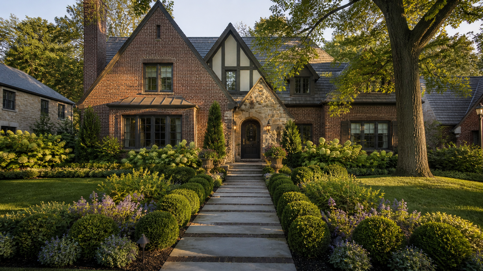 Brick house with a stone arched doorway, manicured hedges, and a stone walkway leading to the front door, flanked by lush landscaping.